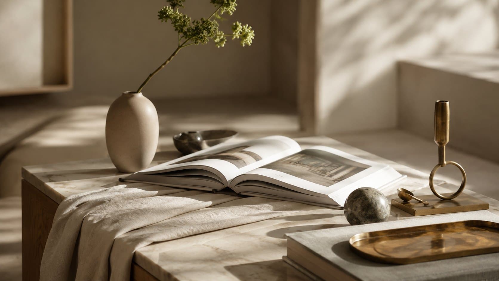 A quiet-luxury still life of linen, marble, oak and brass with an open art book